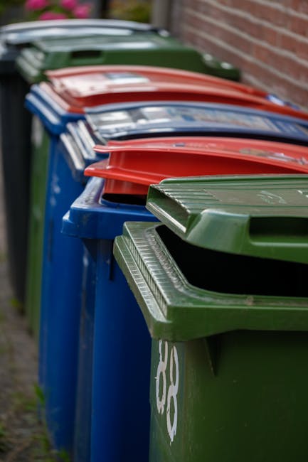 A pile of mixed waste debris is seen on the side of a paved outdoor area, consisting of black plastic rubbish bags, a yellow plastic container, and a discarded car tire with a worn beige fabric coveri